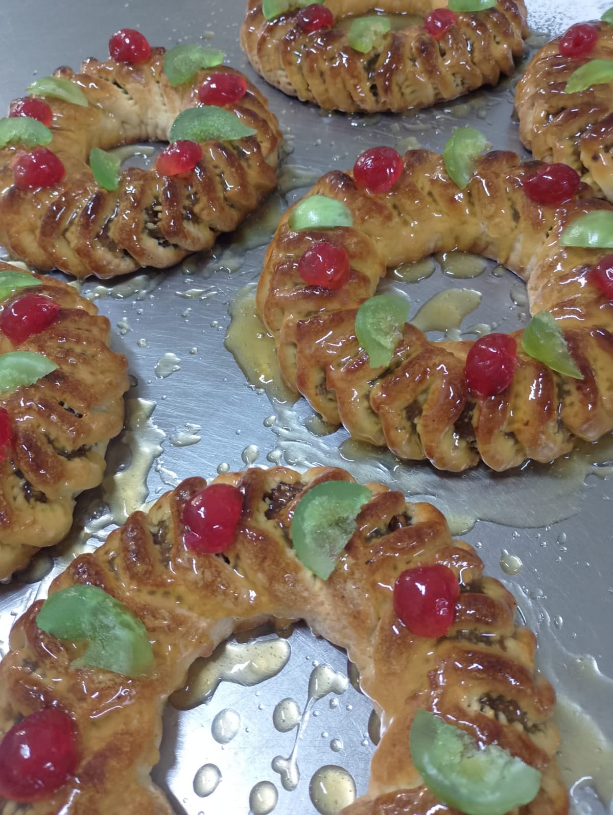 Vassoio di ciambelle di pasta ripiena appena sfornate e lucide di glassa, con la ciliegia candita rossa e il candito verde sopra.