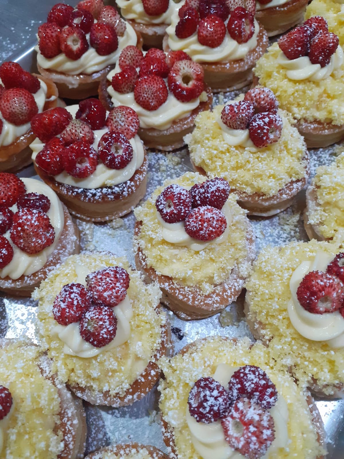 Vassoio di mignon: pasticcini tondi con la crema pasticcera a ciuffo e le fragoline fresche sopra, alcuni rotolati nelle briciole di pan di Spagna, spolverati di zucchero a velo.