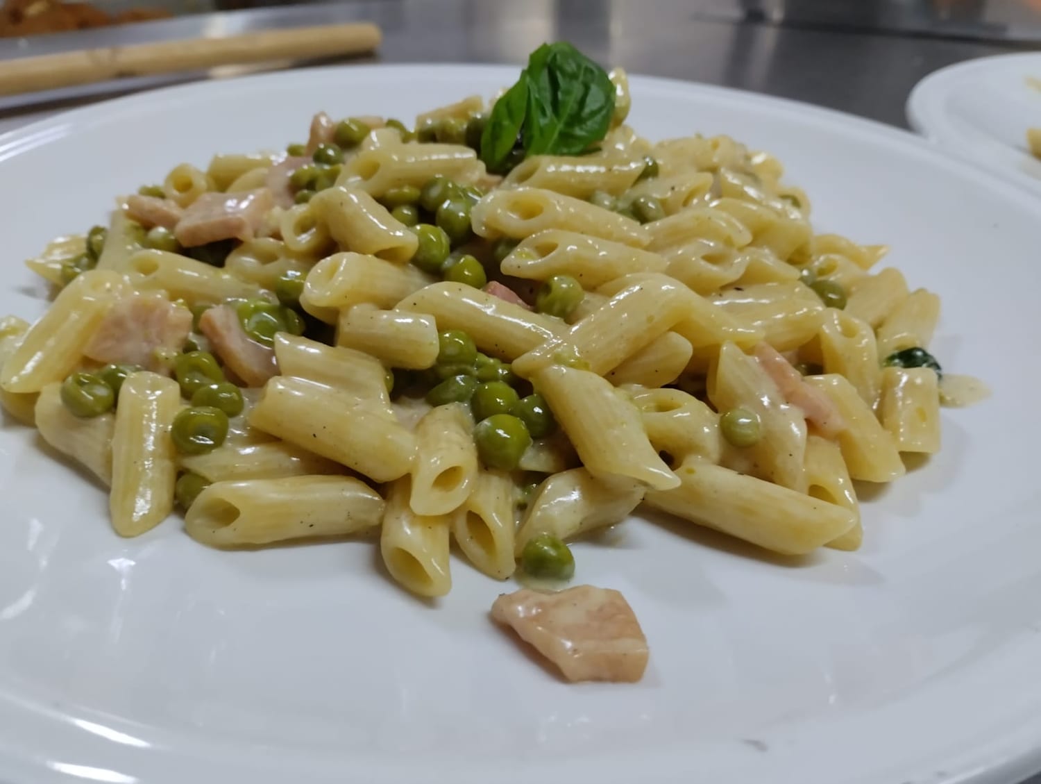 Piatto di penne con piselli e prosciutto in salsa di panna, con una foglia di basilico.