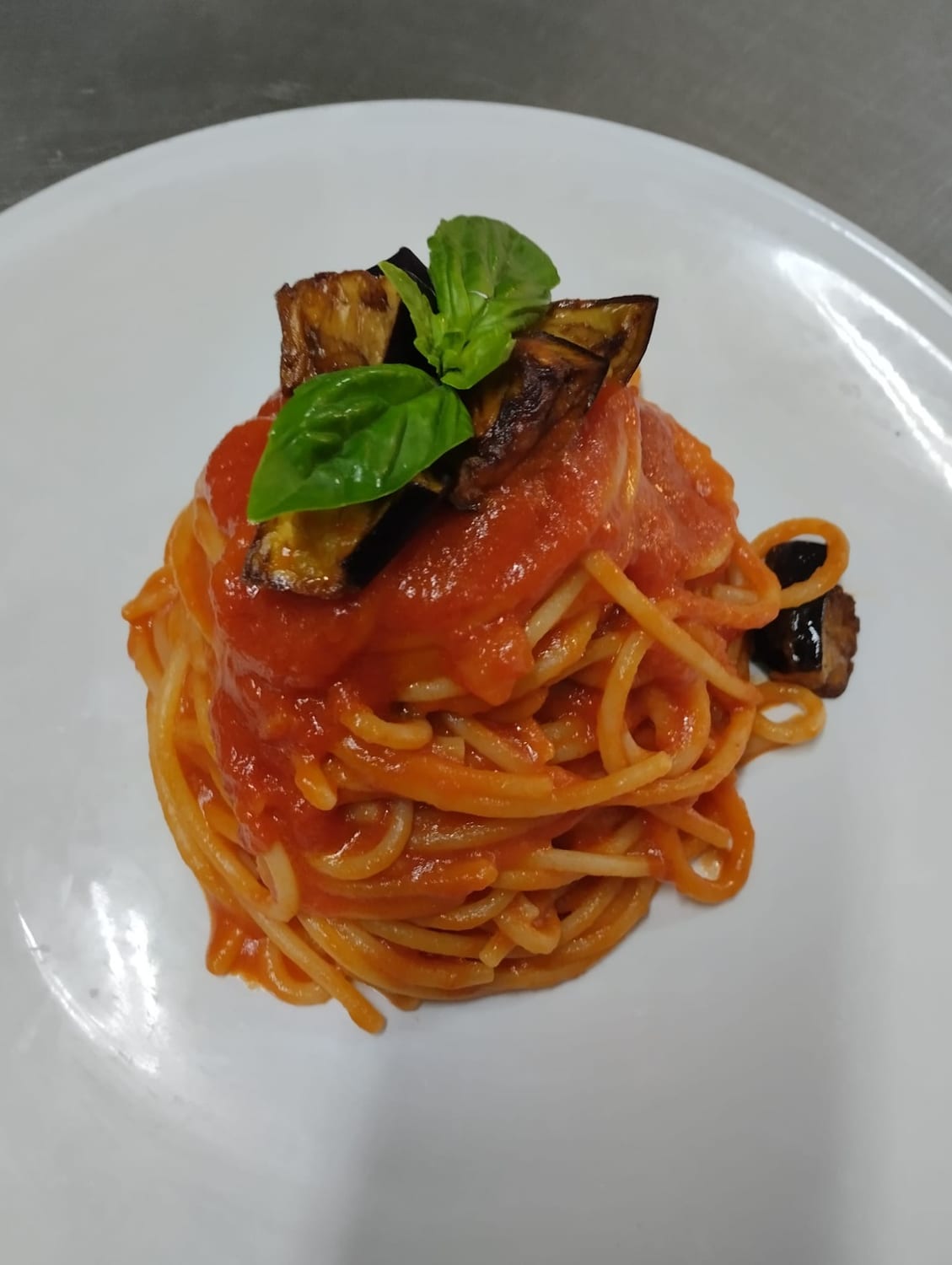 Piatto di spaghetti al pomodoro con melanzane fritte e basilico fresco.