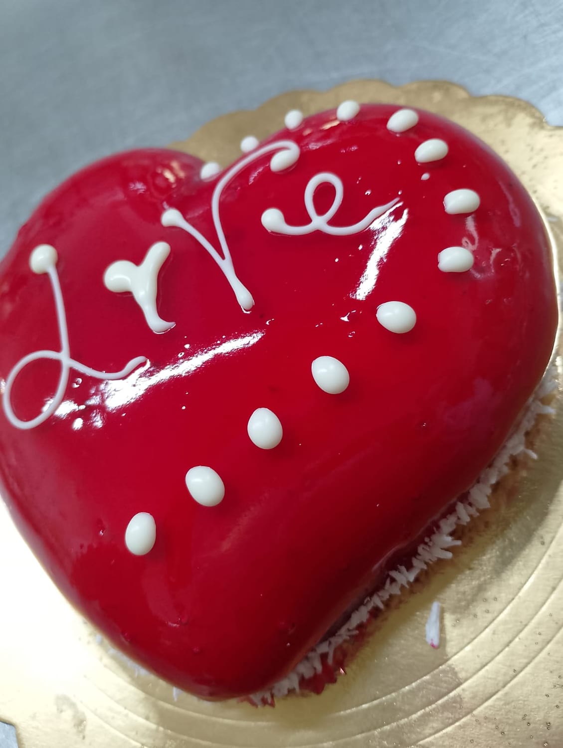 Torta a cuore con glassa rossa lucida, decorata a mano con la panna bianca, sul vassoio dorato.