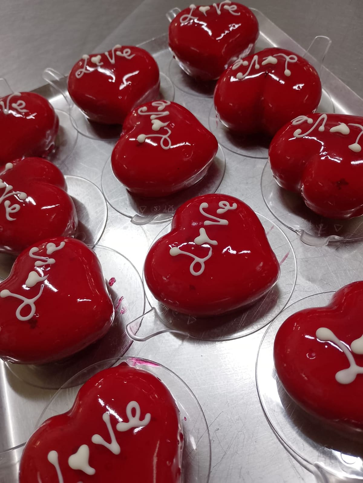 Vassoio di cuori glassati di rosso lucido, ognuno con la scritta Love tirata a mano in cioccolato bianco.